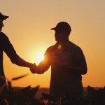 Two farmers talk on the field, then shake hands. Use a tablet